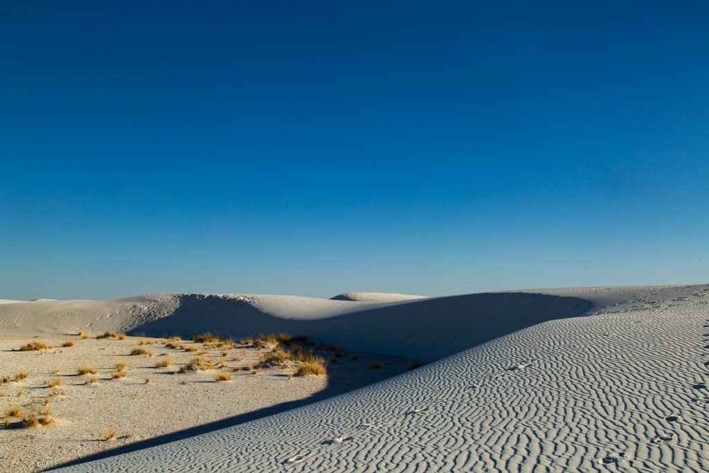 Wide landscape with blue sky, dunes with ripples, and a pair of footprints